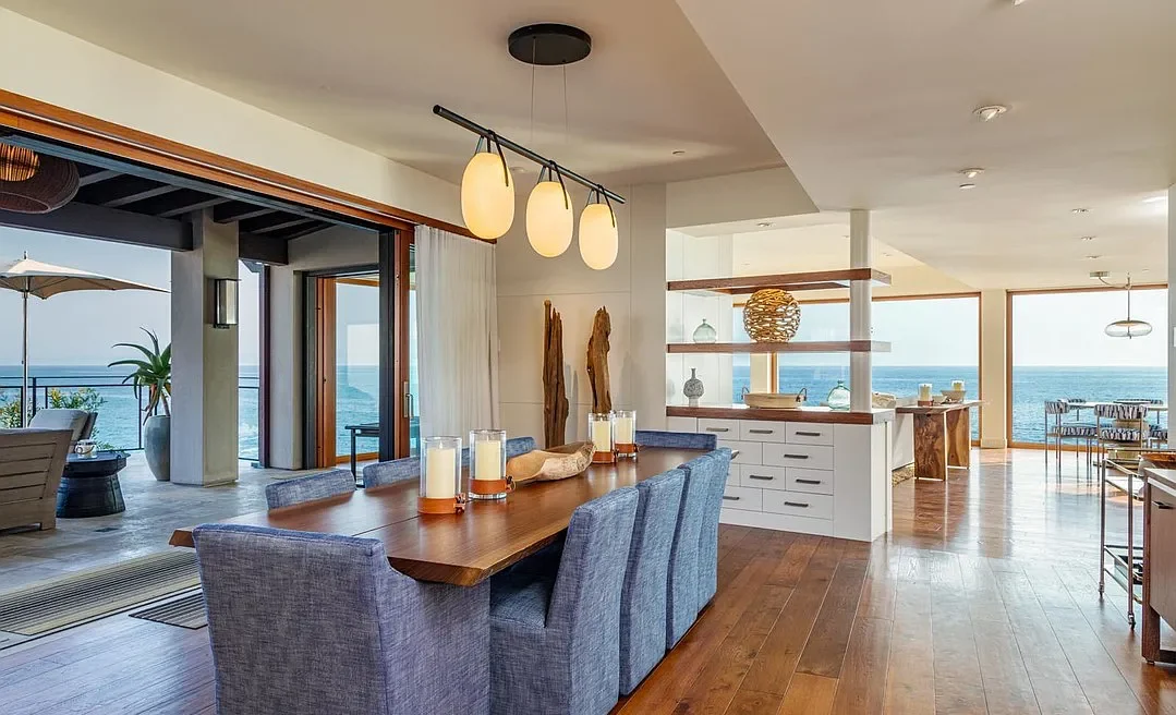 A dining room with a table and chairs, and a view of the ocean.